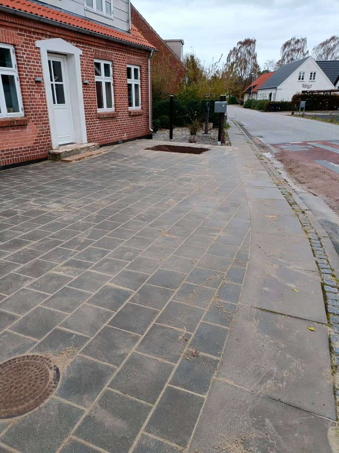 Der er lige blevet lagt fliser ude foran en rød bygning med en hvid dør.