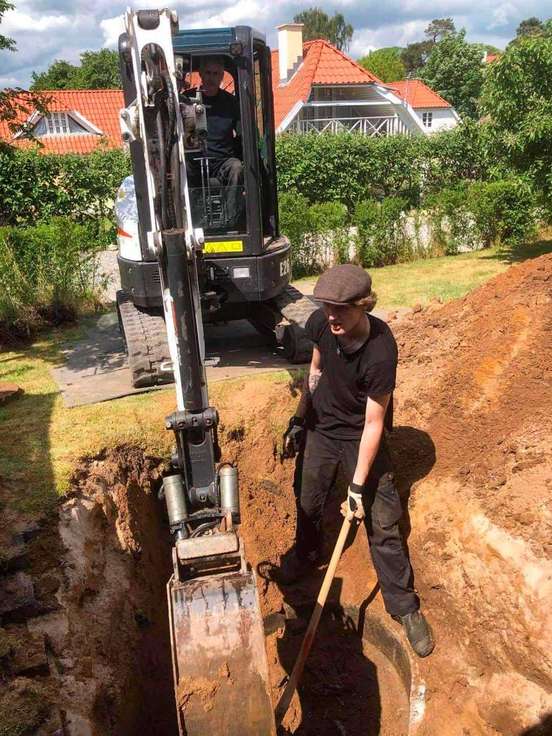 To medarbejdere arbejder sammen og bruger en gravko og en skovl.