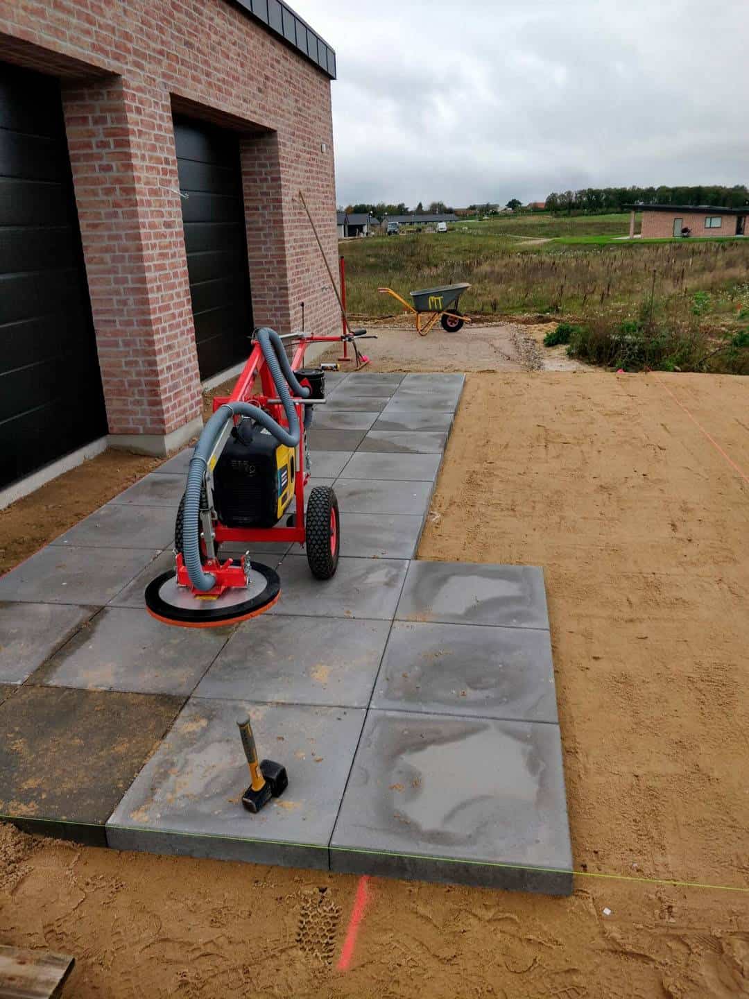 En flisevibreringsmaskine bruges til at lægge fliser ved siden af et hus.